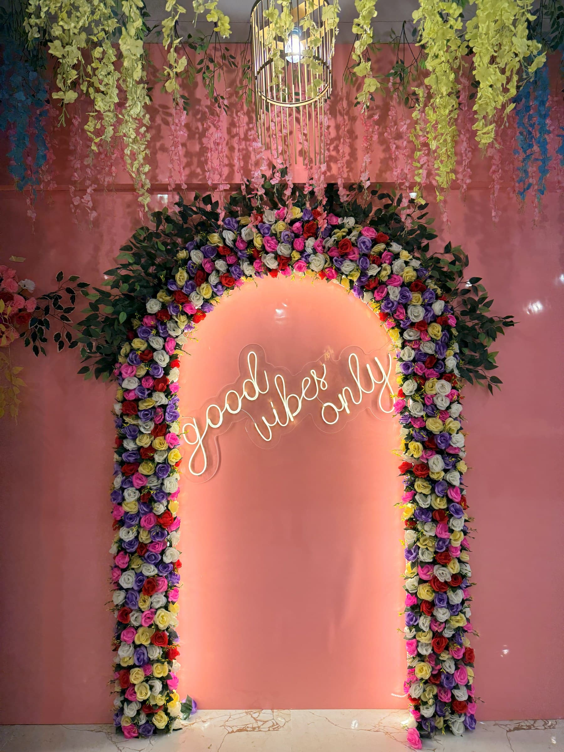 A rose-covered arch lit by a Good Vibes Only neon sign