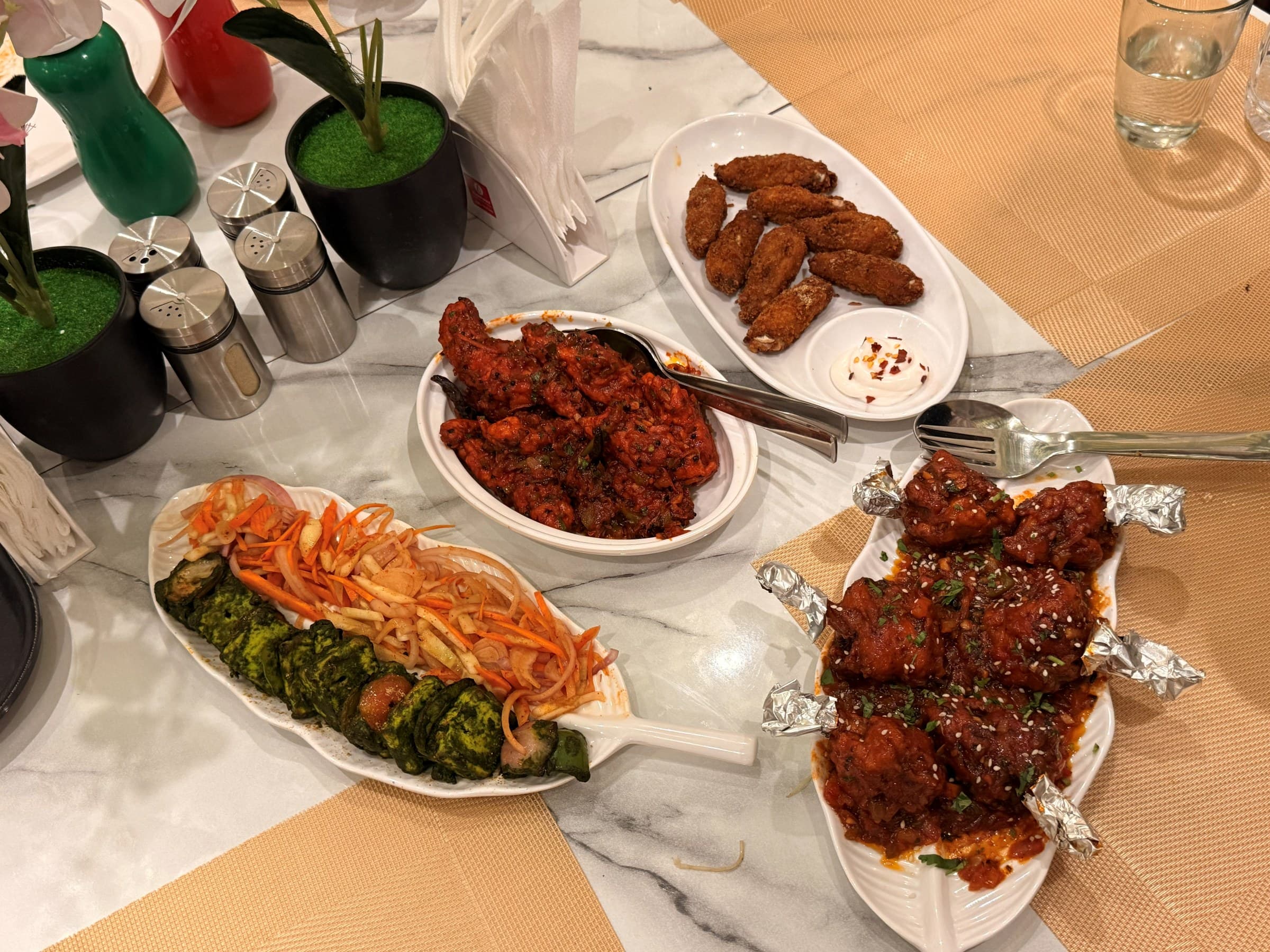A table spread of starters: paneer tikka, chilli chicken and crisp fried wings